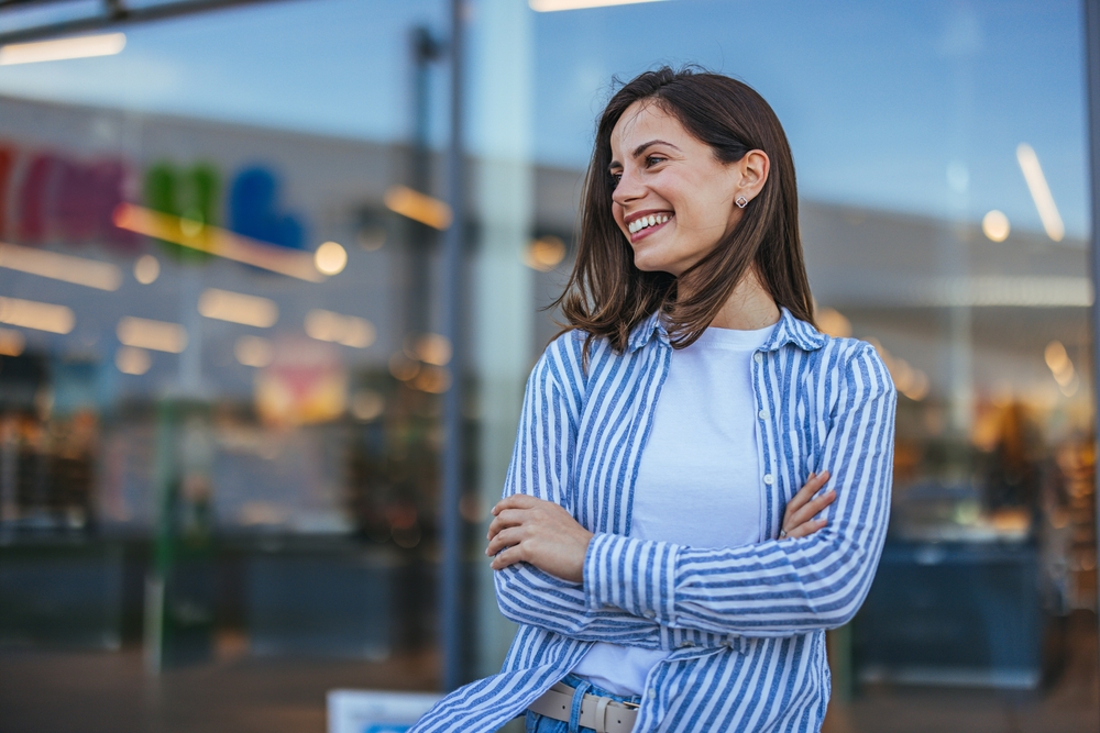 Friendly patient smiling outdoors while holding a phone near dental care services – dentist williamsville ny