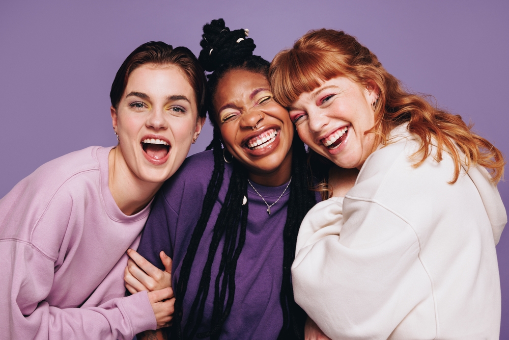 Group of three women laughing and smiling together against a colorful background, symbolizing comfort, confidence, and a welcoming dental care experience – dentist williamsville ny