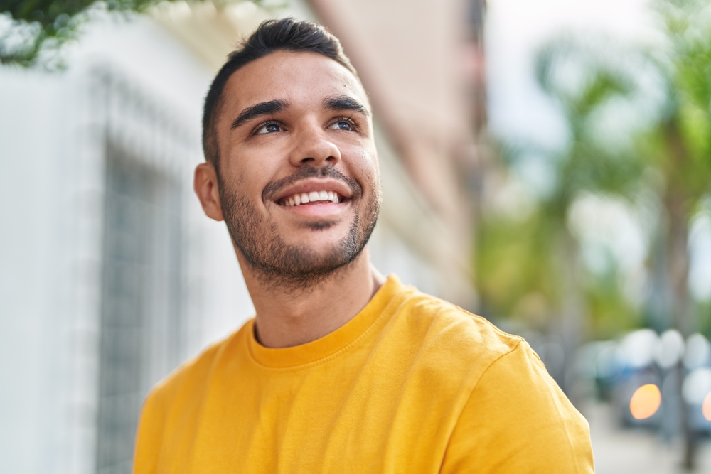 Friendly patient smiling outdoors while holding a phone near dental care services – dentist williamsville ny